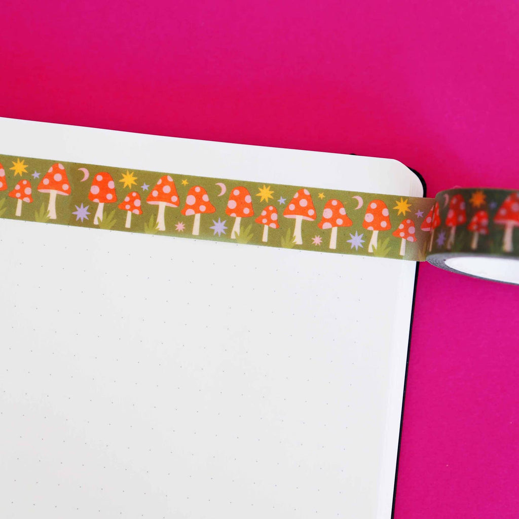 Washi tape with olive green background and images of toadstools in red with pink dots and yellow and lilac bursts and pink moons. 