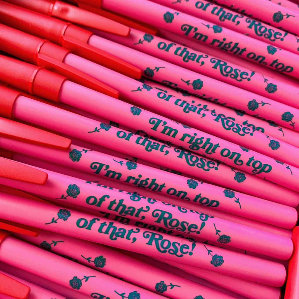 Pink pen barrel with red cap with blue text says, "I'm right on top of that Rose!" with blue roses. 