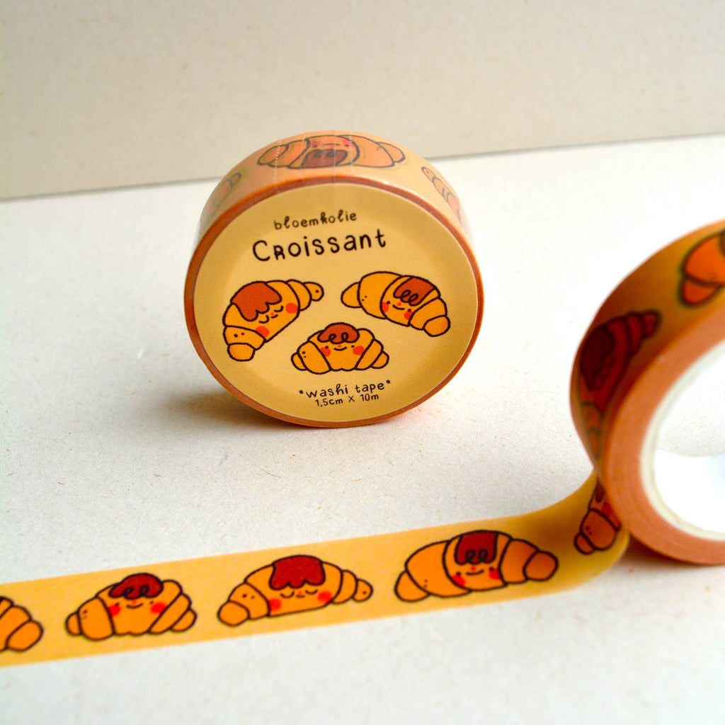 Image of roll of washi tape with yellow background and images of golden croissants with brown "hair" and red cheek circles.