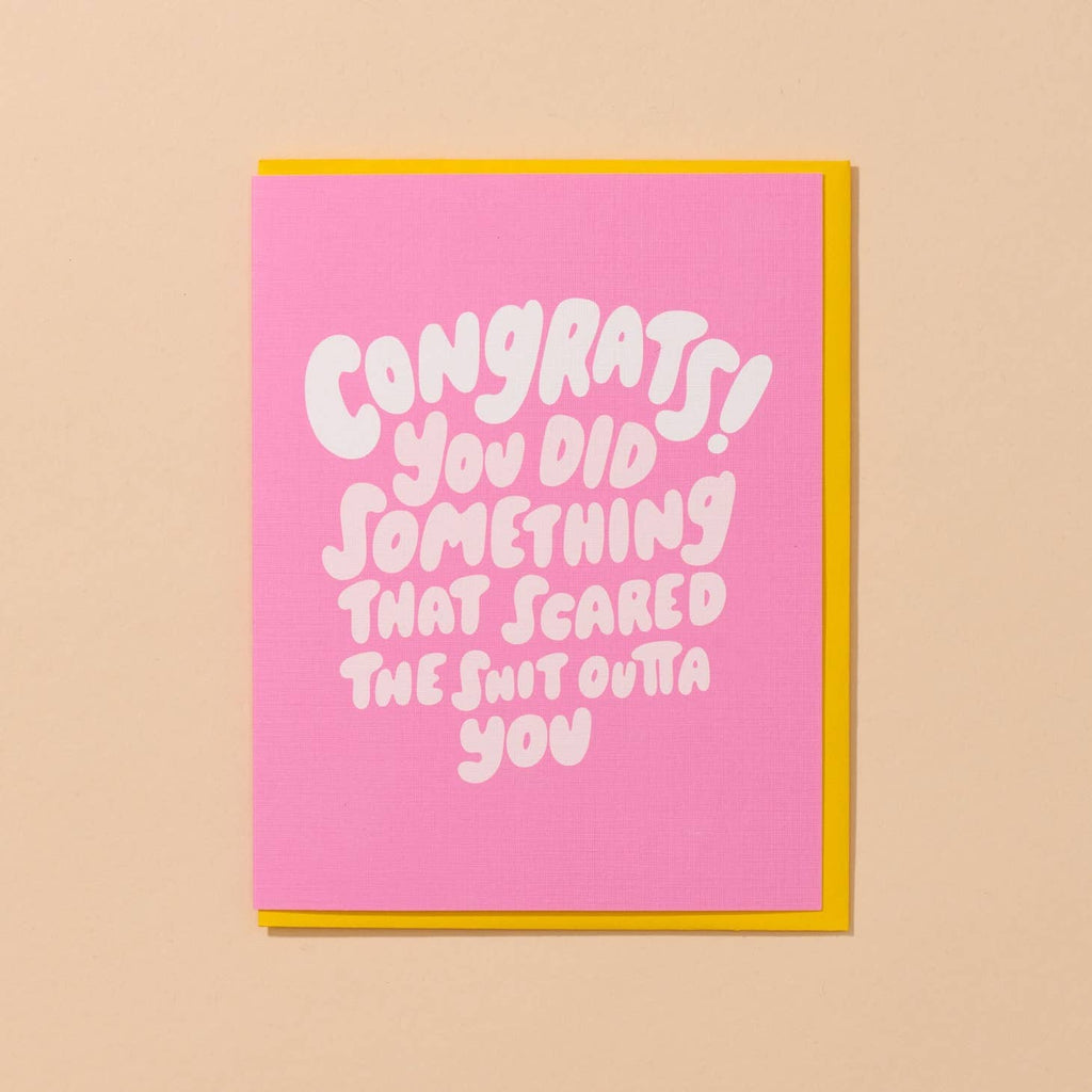 Greeting card with pink background with white puffy text says, "Congrats! You did something that scared the shit outta you". Yellow envelope included. 