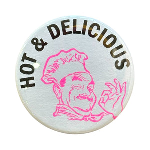 Image of metal button with white background with image of a chef in hot pink outline and black text says, "Hot & Delicious". 