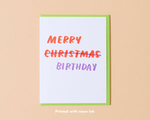 Image of card with white background with neon orange text says, "Merry Christmas" with lilac text that crosses out Christmas and text says, "Birthday". Neon green envelope included. 