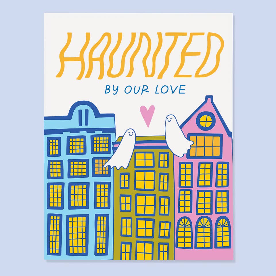White background with images of three buildings in pink, green and blue with two ghosts floating with a pink heart between them. Yellow and blue text says, “Haunted by our love”. Envelope included. 