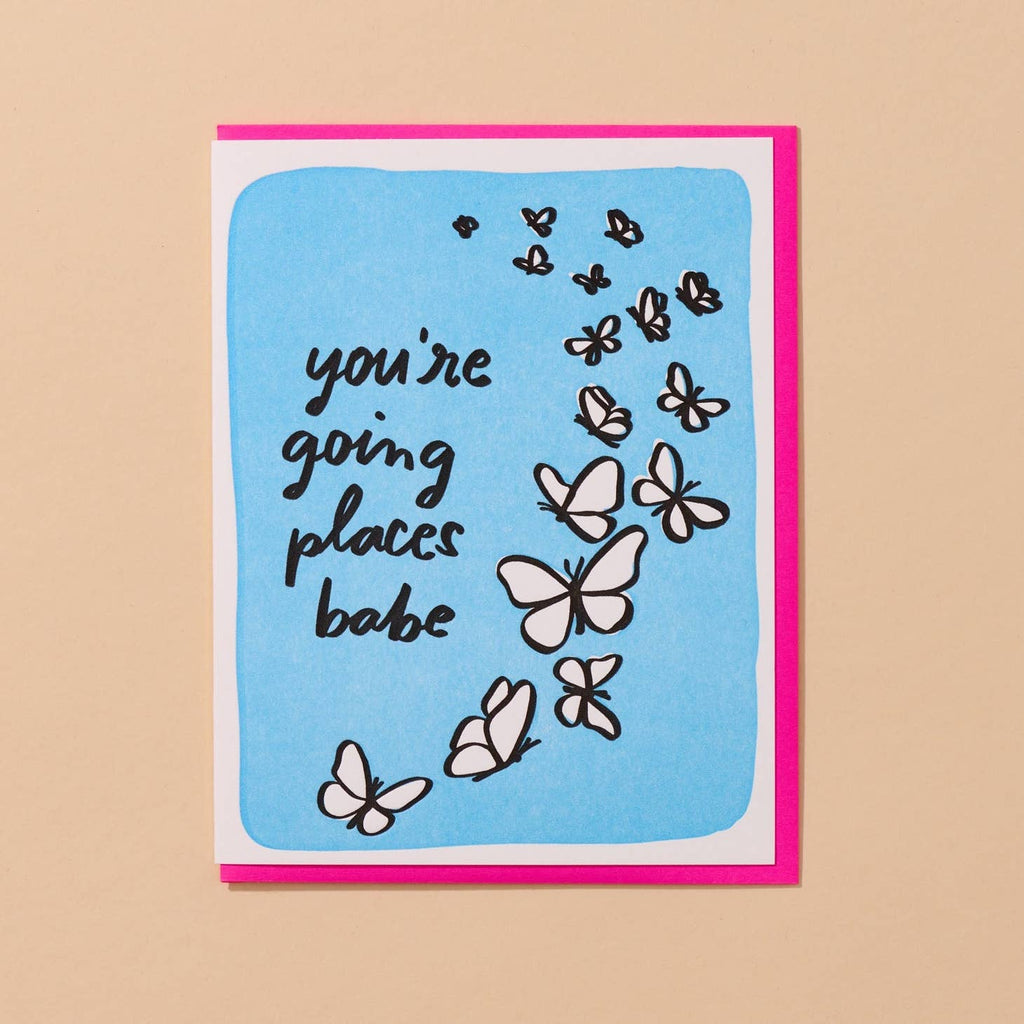 Greeting card with blue background with white frame and black outined butterflies with black text says, "You're going places babe". Neon pink envelope included. 