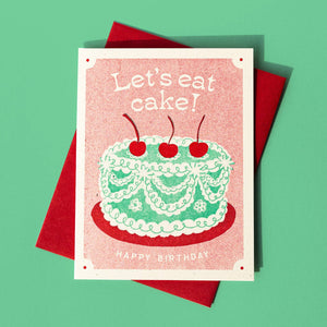 Greeting card with ivory and red background with image of an aqua cake with three red cherries on top with cream text says, "Let's eat cake!" and "Happy birthday". Red envelope included. 