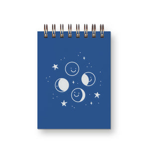 Pocket notebook with blue cover and white images of phases of moon with coiled binding at top.