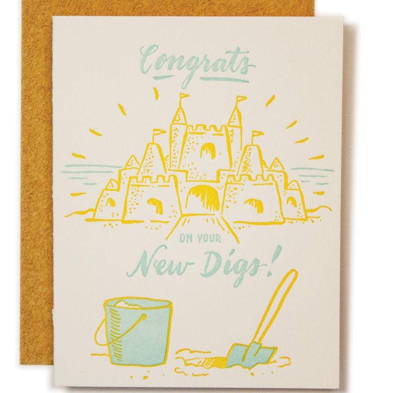 Ivory background with image of a yellow sandcastle  with blue bucket and shovel and blue text says, "Congrats on your new digs!". Kraft envelope included.