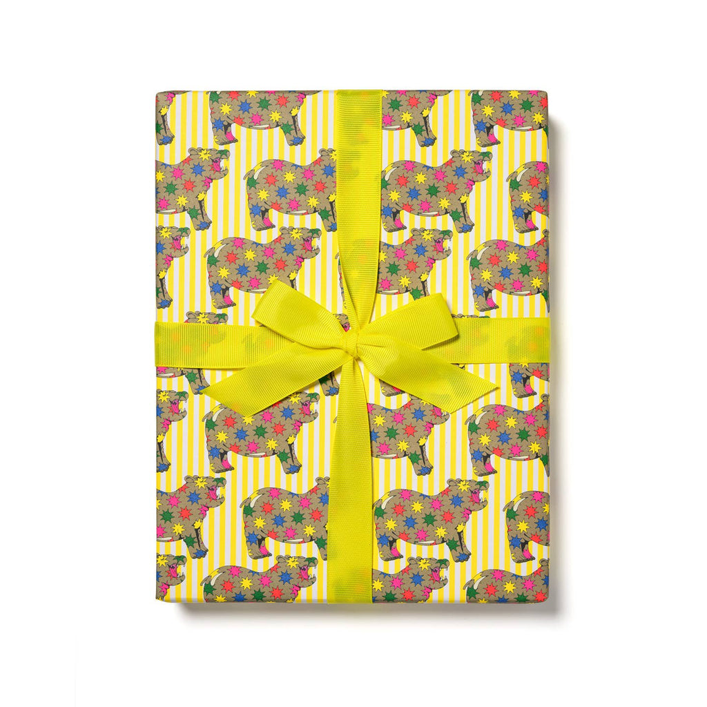 Gift wrap with yellow and white stripe background and images of brown hippo covered in rainbow color star bursts. 