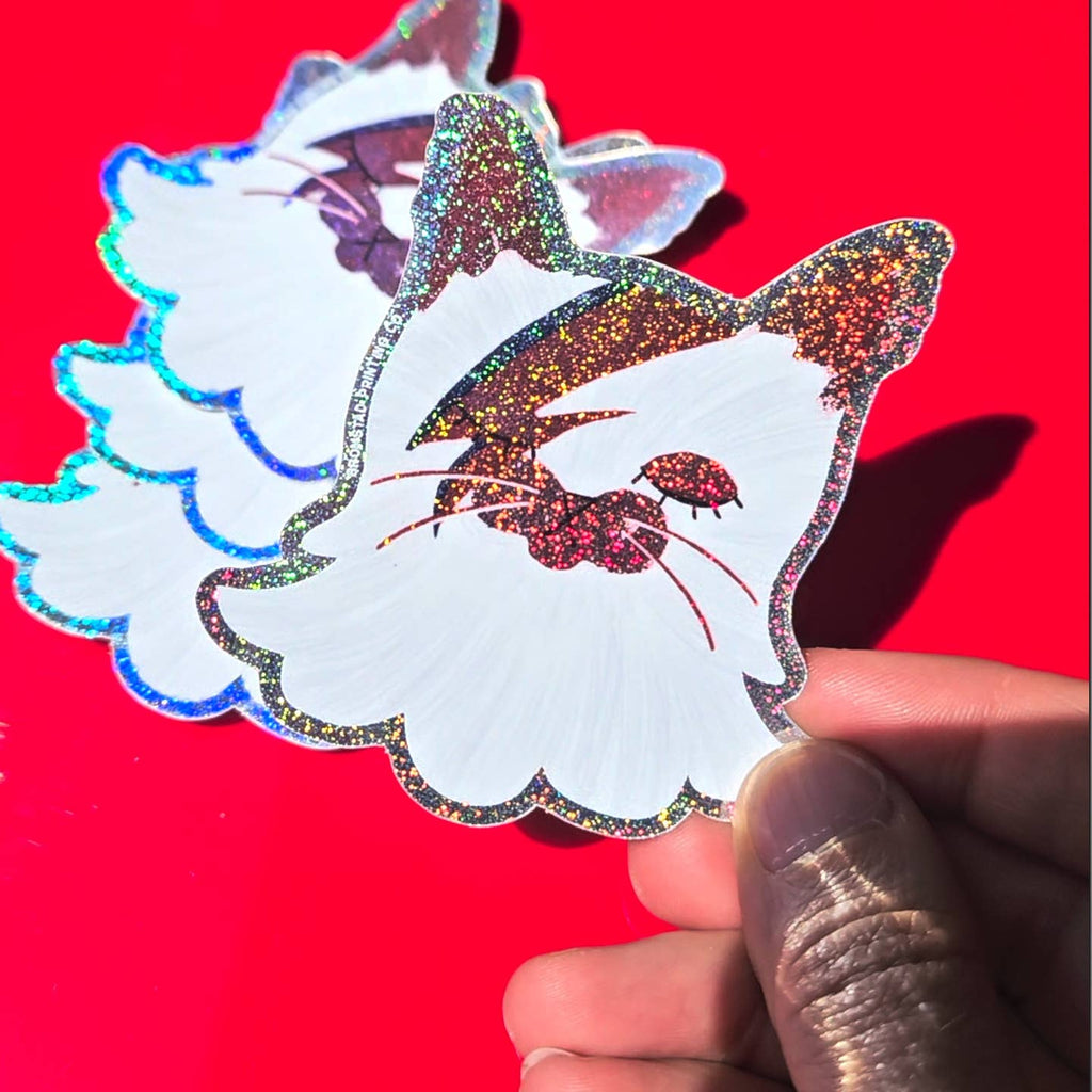 Decorative sticker in the image of a white cat with a lightening bolt on it's face and glitter outlining. 