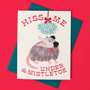 Greeting card with image of a possum under mistletoe with red text says, "Hiss me under the mistletoe". Green envelope included.