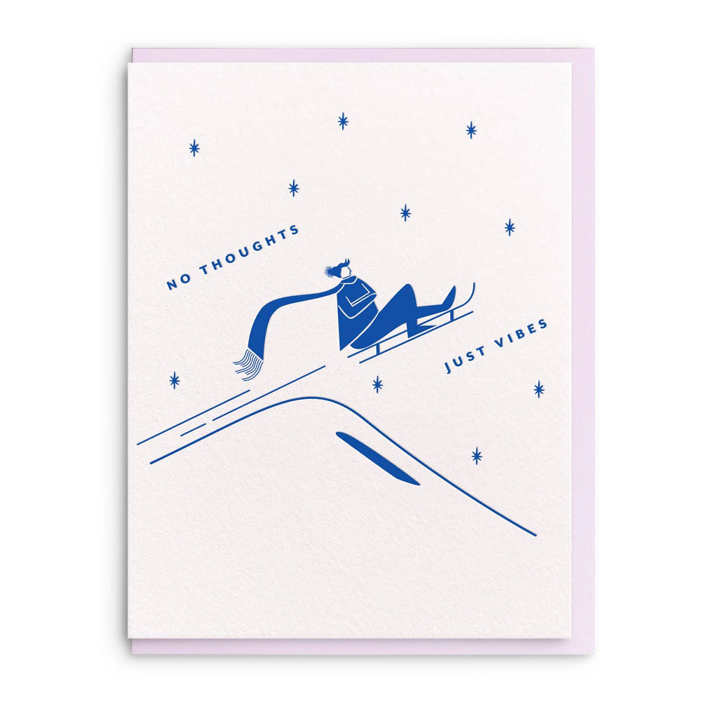 Greeting card with white background and image of person riding on a sled in blue ink and text says, "No thoughts, just vibes". Lilac envelope included.