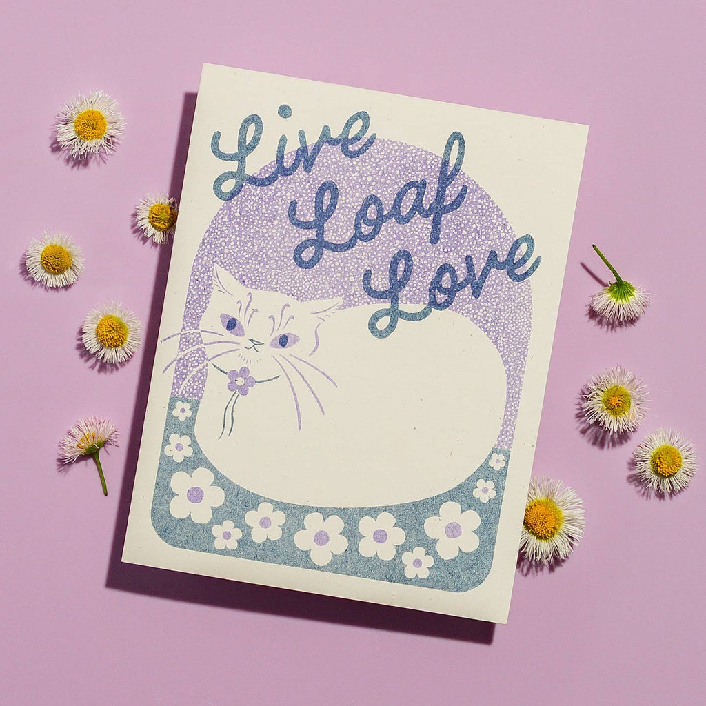 Greeting card with cream background and image of a cat in loaf position with blue text says, "Live loaf love". Envelope included.