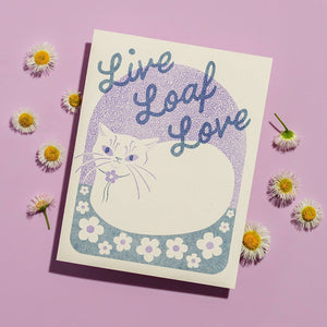 Greeting card with cream background and image of a cat in loaf position with blue text says, "Live loaf love". Envelope included.