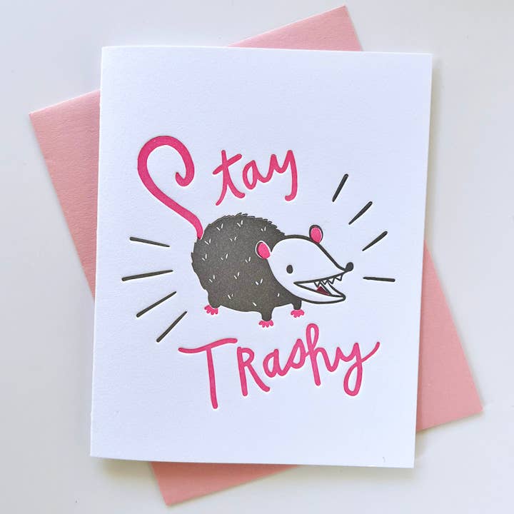 Greeting card with white background and image of grey, white and pink possum with pink text says, "Stay trashy". Pink envelope included. 