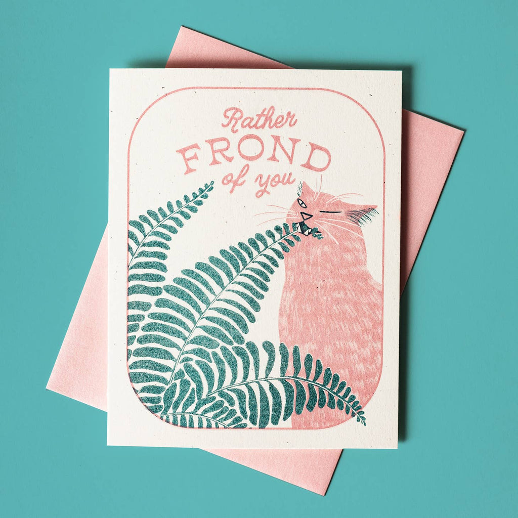 Ivory background with image of a pink cat with a teal fern frond. Pink text says, "Rather frond of you". Pink envelope is included, 