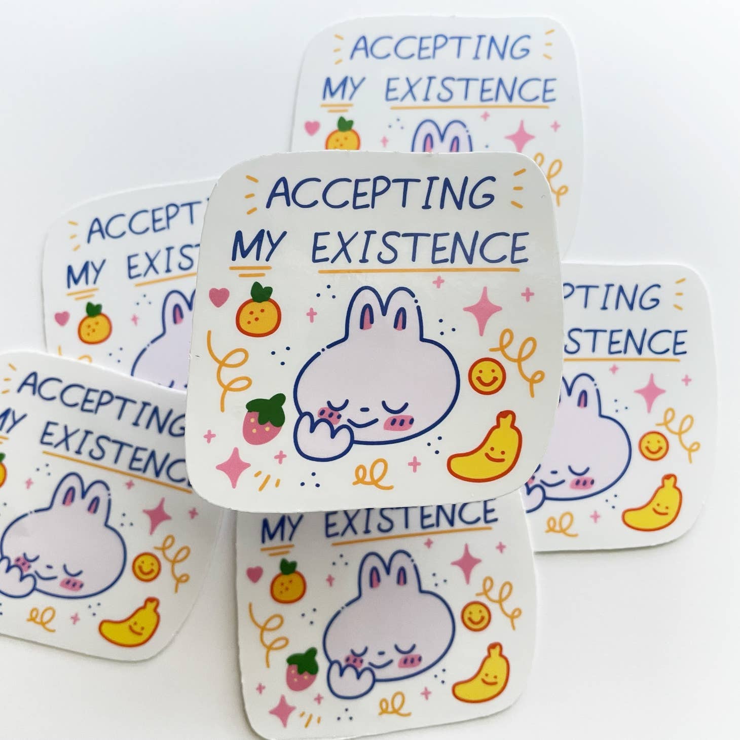Sticker with white background and image of bunny with pink doodles and yellow banana and smiley date.  Blue text says, "Accepting my existence", 