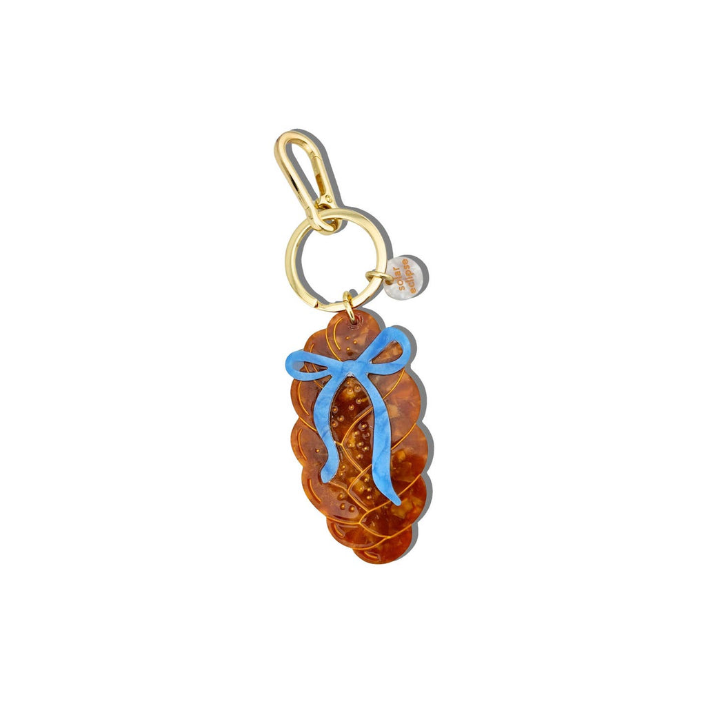 Image of keychain charm in the shape of a loaf of Challah bread and a blue bow. Gold colored ring and clip. 
