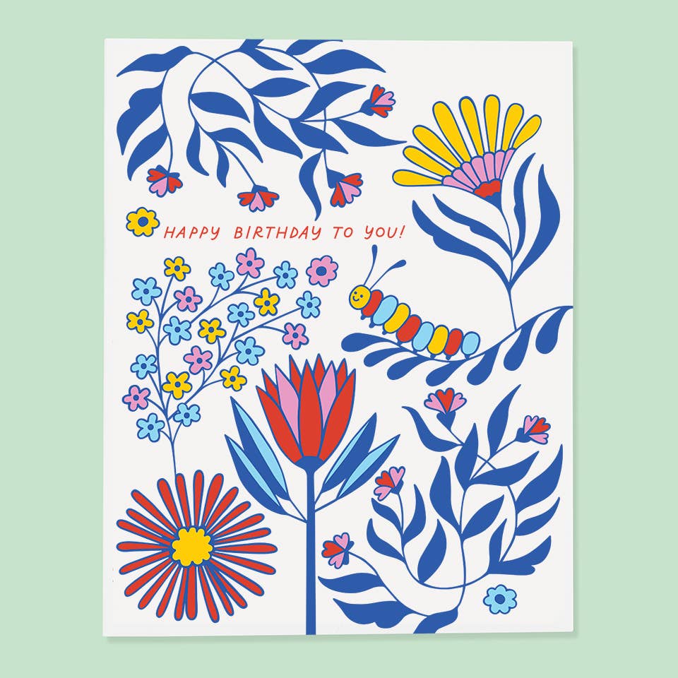 White background with images of blue, pink, yellow and red flowers. Red text says, “Happy birthday to you!”. White envelope included.  