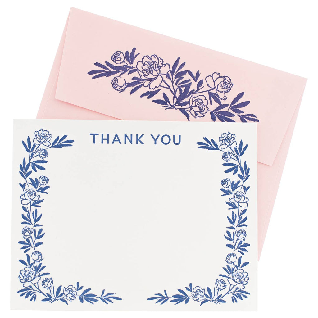Image of notecard with white background and blue flower border with blue text says, “Thank you”. Pink envelopes with blue flowers on back flap. 