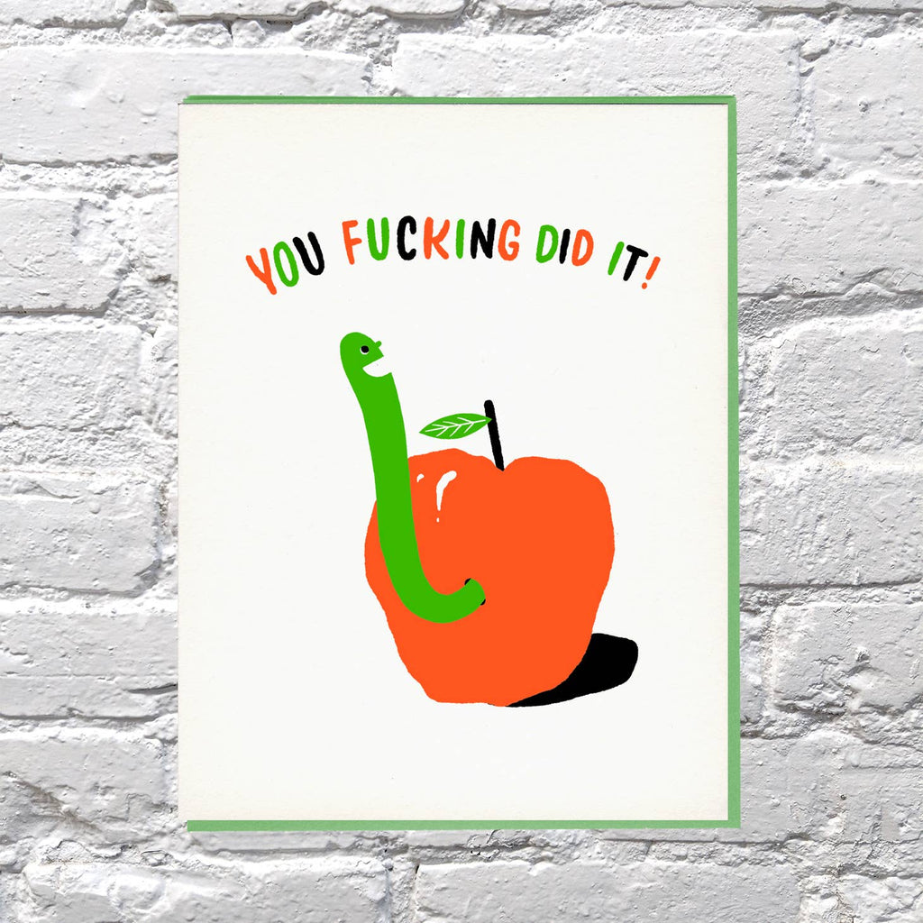 Greeting card with image of a red apple with a green worm coming out of it, Red, green and black text says, "You fucking did it!". Green envelope included. 