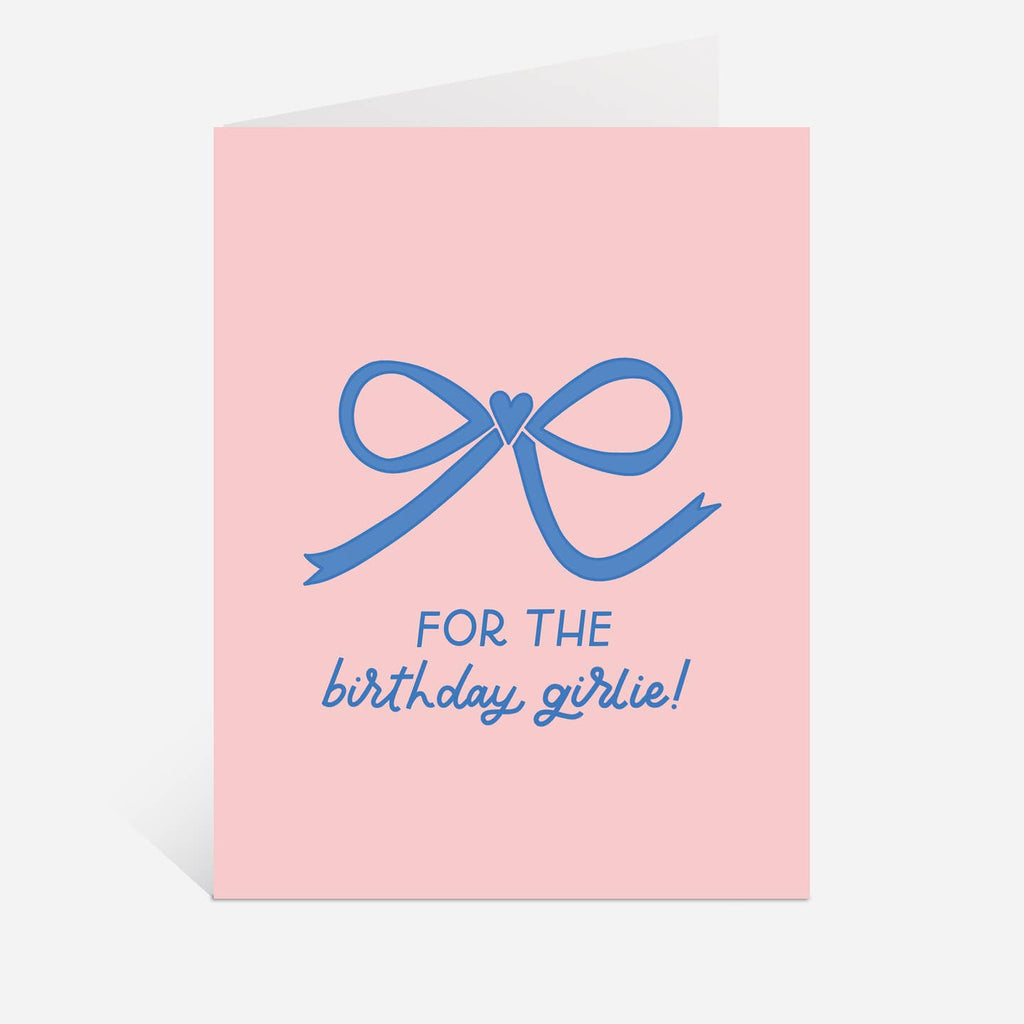 Greeting card with pink background and image of a blue bow with blue text says, "For the birthday girlie!". Envelope included. 