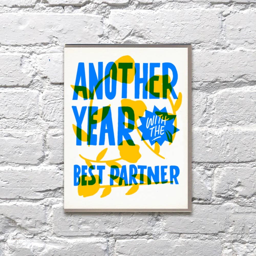 Greeting card with white background and blue text over yellow flowers says, "Another year with the best partner". Kraft envelope included.