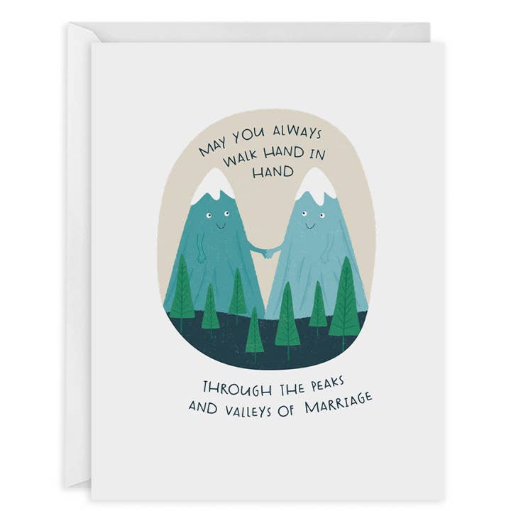 White background with tan circle, inside two snowcapped mountains in teal and aqua are holding hands in back of a group pf green trees. Black text says, “May you always walk hand in hand through the peaks and valleys of marriage”. A white envelope is included.     