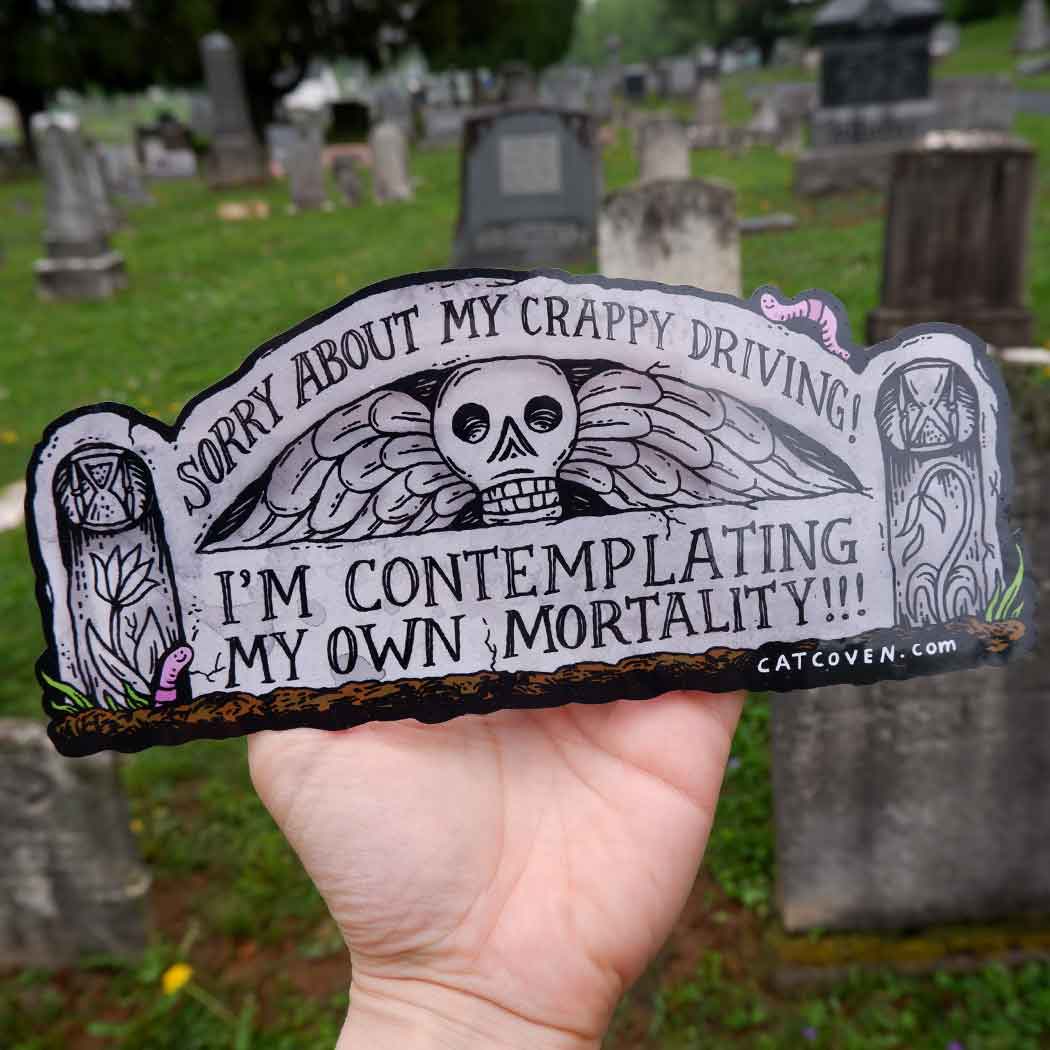 Decorative sticker with grey background and shaped like a gravestone. Black text says, "Sorry about my crappy driving!, I'm contemplating my own mortality!!!". 