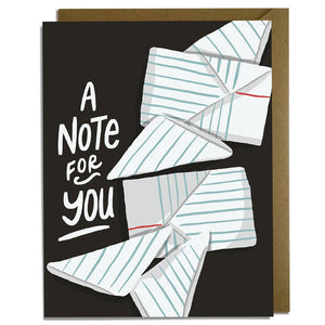 Greeting card with black background and images of folded notes on notebook paper. White text says, "A note for you". Kraft envelope for you.
