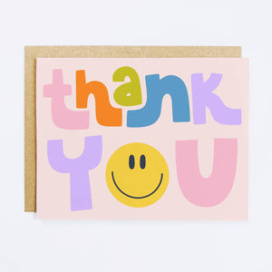 Pink background with multicolored text says, "Thank you" with yellow smiley face as the "O". Kraft envelope included.