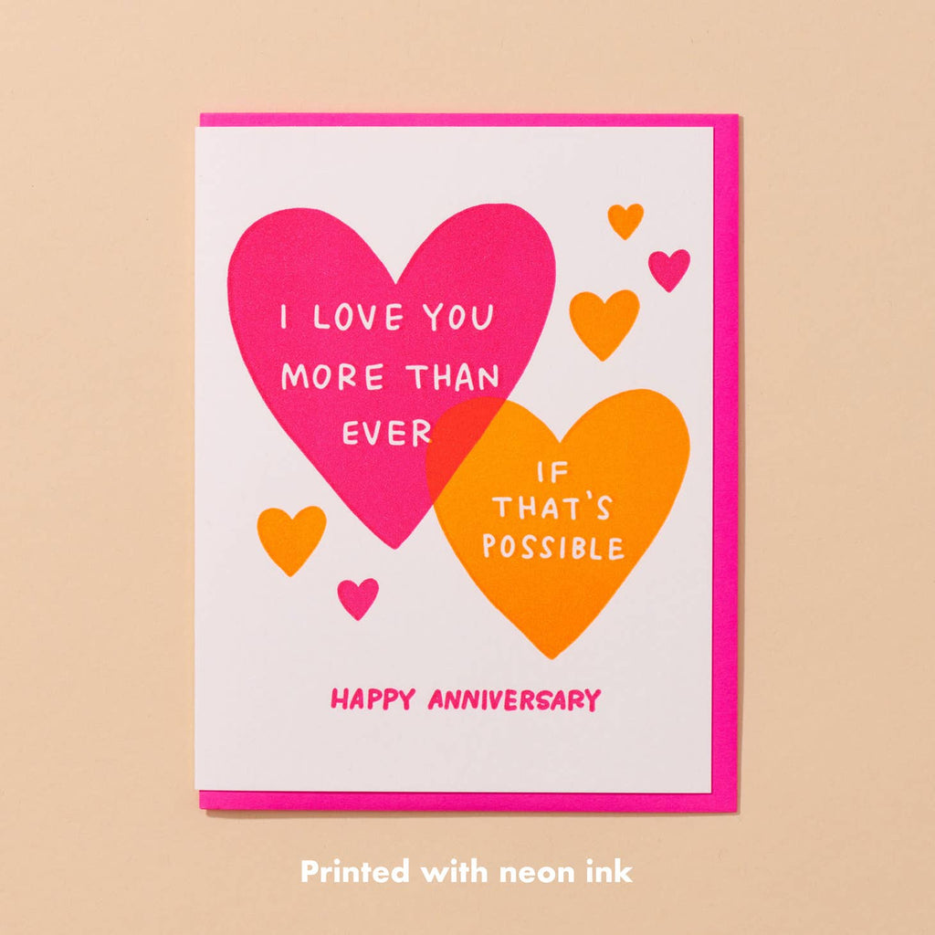Greeting card with white background and images of pink heart with white text says, "I love you more than ever" and orange heart with white text says, "If that's possible" and pink text says, "Happy Anniversary". Bright pink envelope included. 