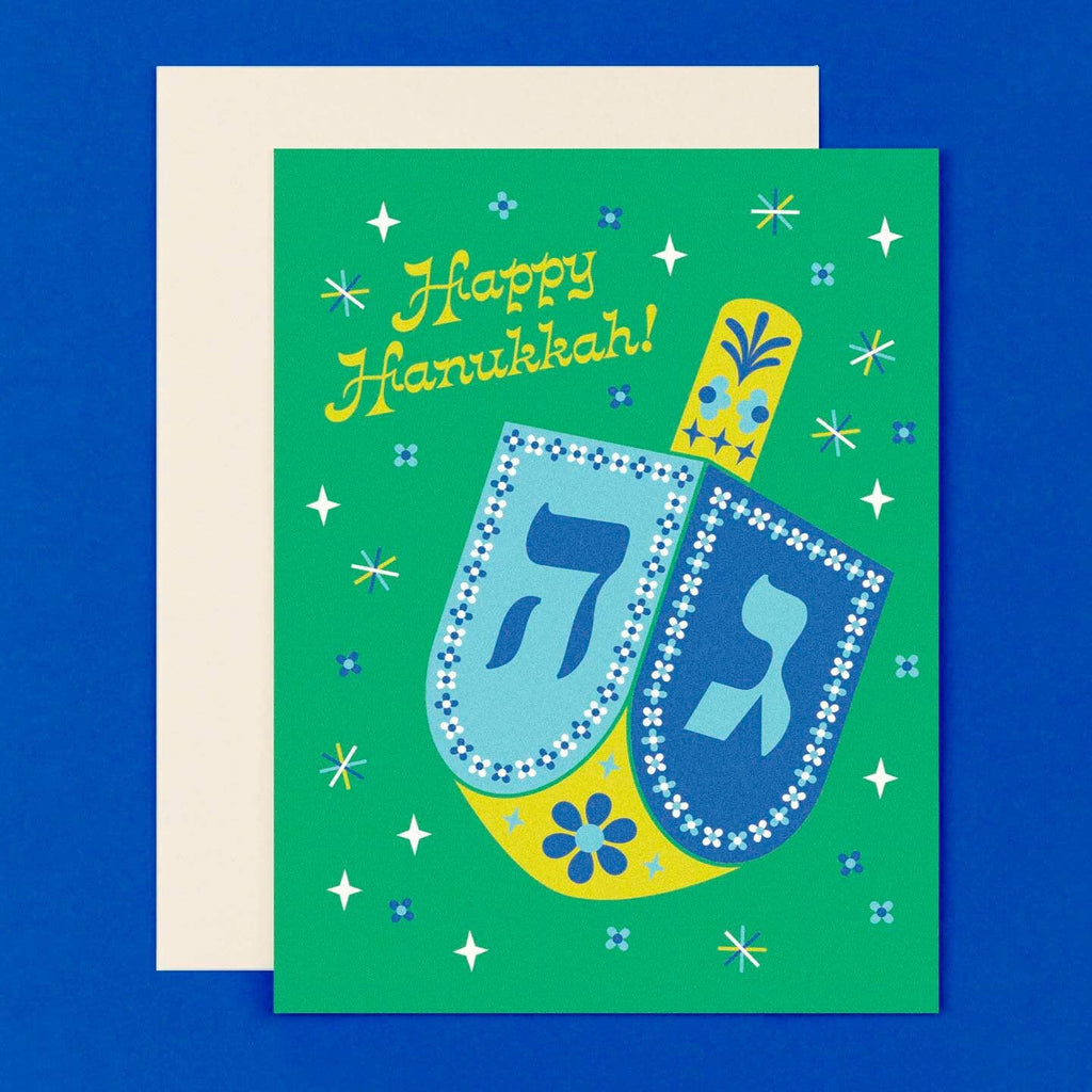 Greeting card with green background with image of a blue, white and chartreuse dreidel with text says, "Happy Hanukkah!". Envelope included. 