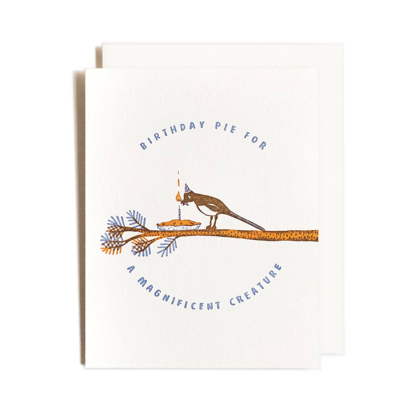 Greeting card with cream background and image of brown magpie holding a lighted match and lighting a candle on a pie sitting on a tree branch. Blue text says, "Birthday pie for a magnificent creature.  Cream envelope included. 
