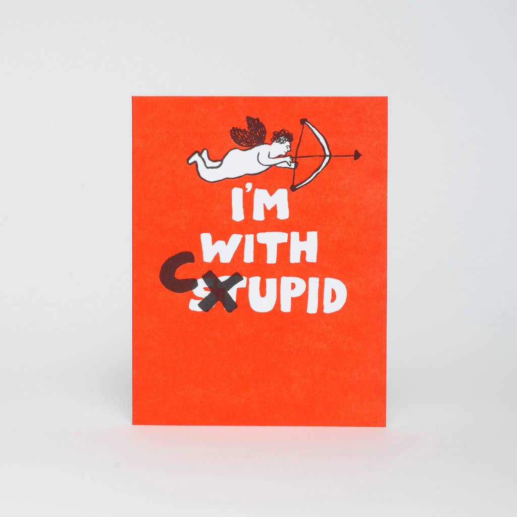 Greeting card with red background and image of Cupid with a bow and arrow and white text says, "I'm with Stupid" with black text of "X" over the "ST" and "C". Kraft envelope included. 