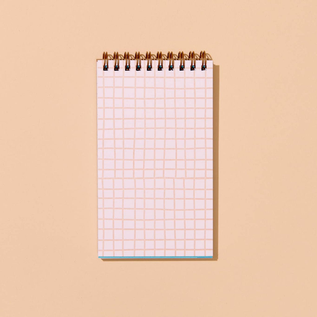 Pocket sized notebook with white background and tan grid lines with coiled binding at top. 