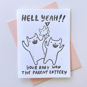 Greeting card with white background and image of three creatures - two adults and a baby holding a heart flag. Grey text says, "Hell yeah!! Your baby won the parent lottery". Pink envelope included. 