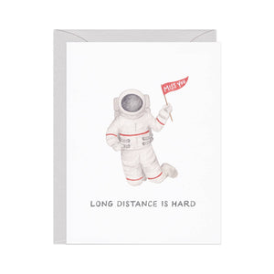 White background with image of an astronaut holding a flag that says, "Miss you". Black text says, "Long distance is hard". Grey envelope is included.