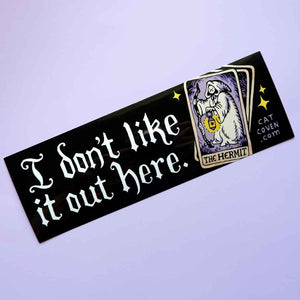Decorative sticker with black background and white text says, "I don't like it out here. Image of a white tarot card with black text says, "the hermit".