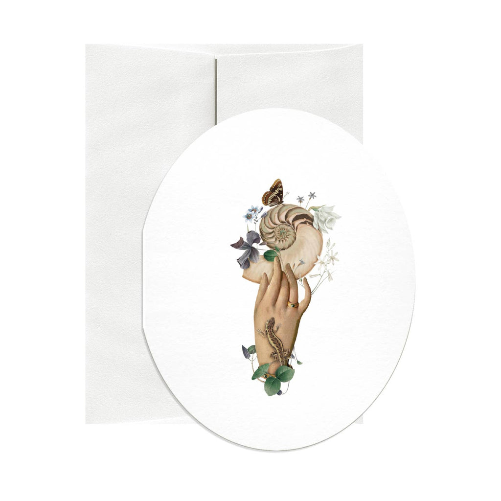 Oval shaped greeting card with white background and image of a hand holding a nautilus shell and flowers. Envelope included. 