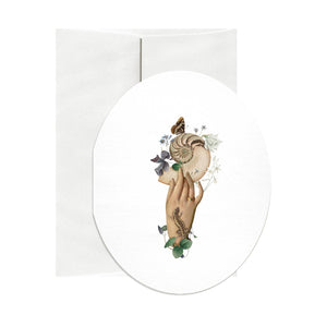 Oval shaped greeting card with white background and image of a hand holding a nautilus shell and flowers. Envelope included. 