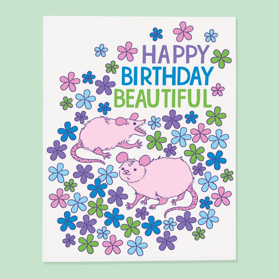 Greeting card with white background and image of two pink possums and purple, blue and green text says, "Happy birthday beautiful". Envelope included.