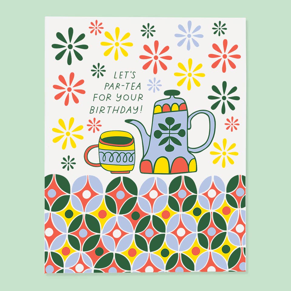 Greeting card with white background and image of teapot and cup with geometric designs in red, yellow, green and blue. Green text says, "Let's par-tea for your birthday!". Envelope included. 