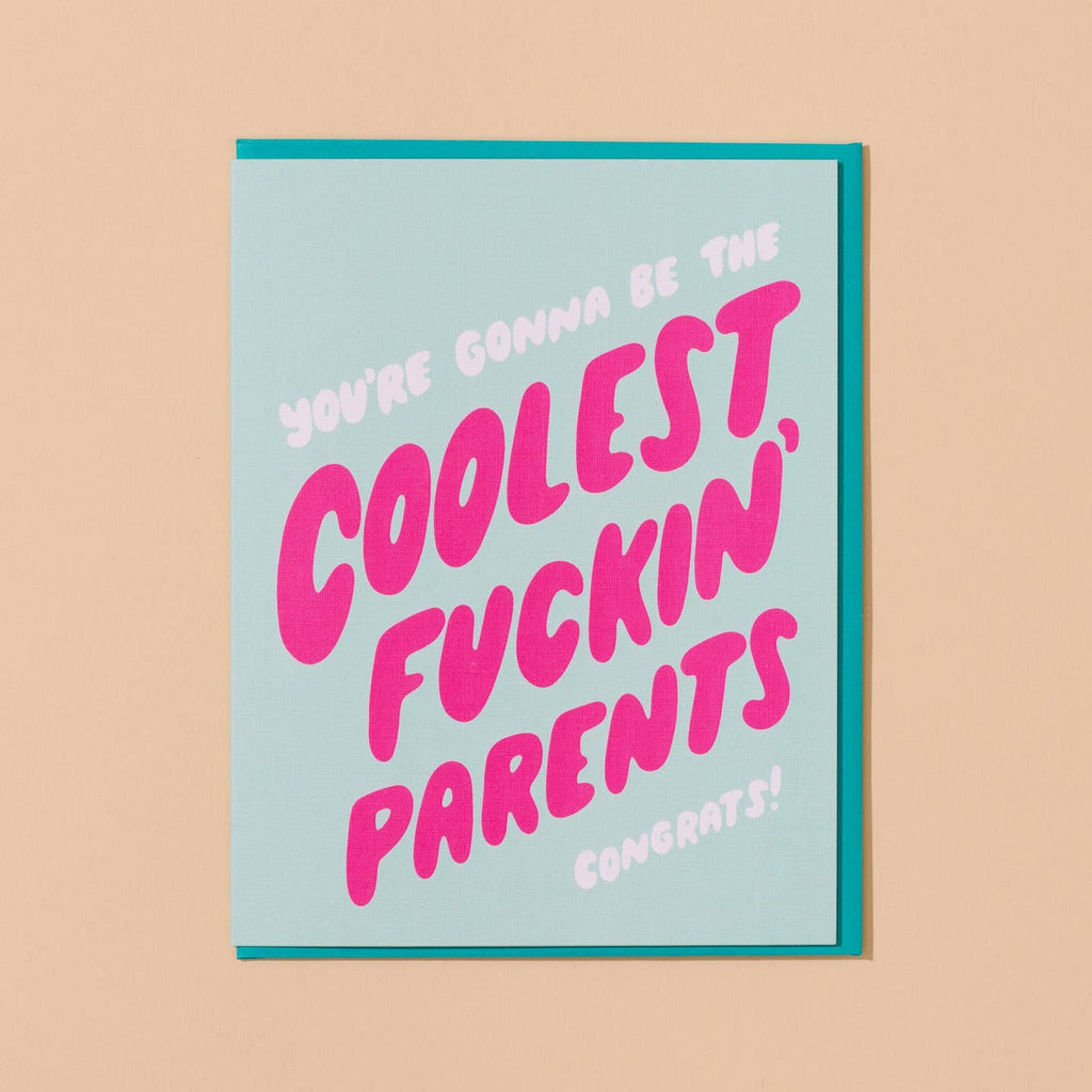 Greeting card with aqua background with white and pink text says, "You're gonna be the coolest, fuckin' parents congrats!". Teal envelope included.