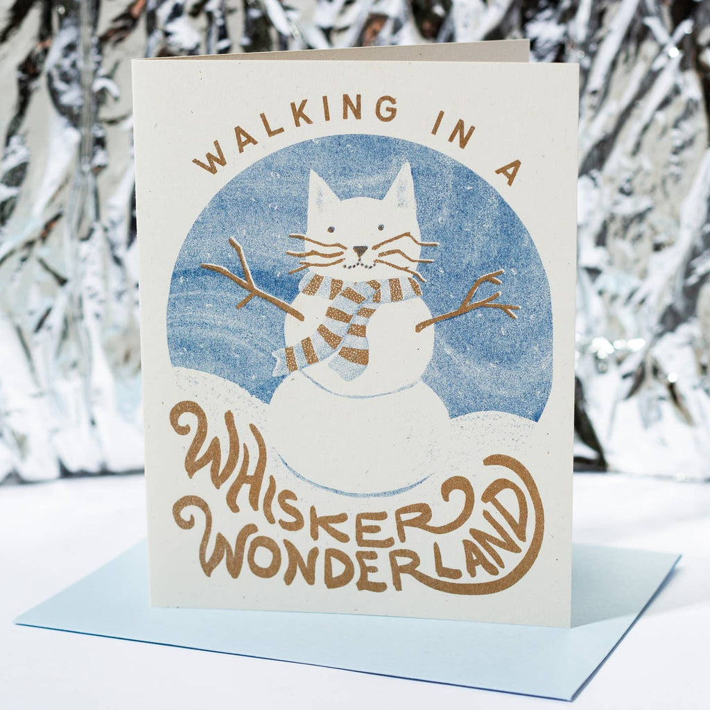 Greeting card with white background and blue circle in center with an image of a cat as a snowman. Brown text says "Walking in a whisker wonderland".  Blue envelope is incuded. 