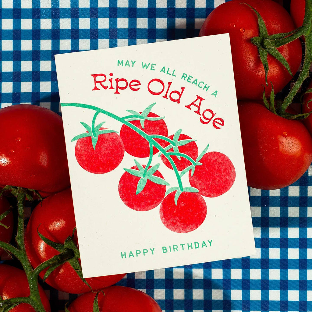 Greeting card with cream background and image of a bunch of red tomatoes and green text says, "May we all reach a ripe old age. Happy Birthday". Envelope included.