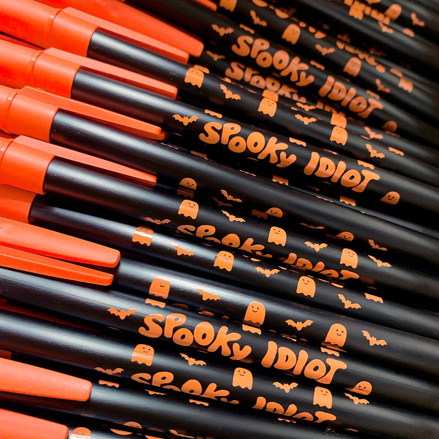 Pen with black barrel with orange cap and orange text says, "Spooky idiot". 