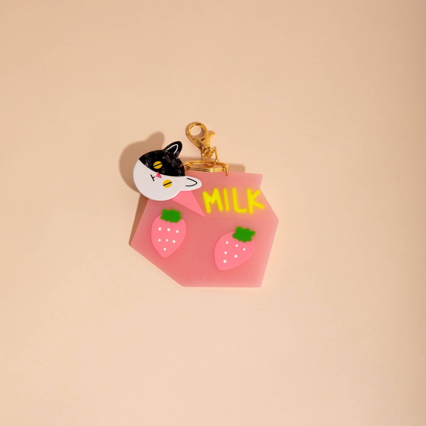 Image of plastic charm in shape of black and white cat face and pink carton of milk with strawberry on side and yellow text says, "Milk". 