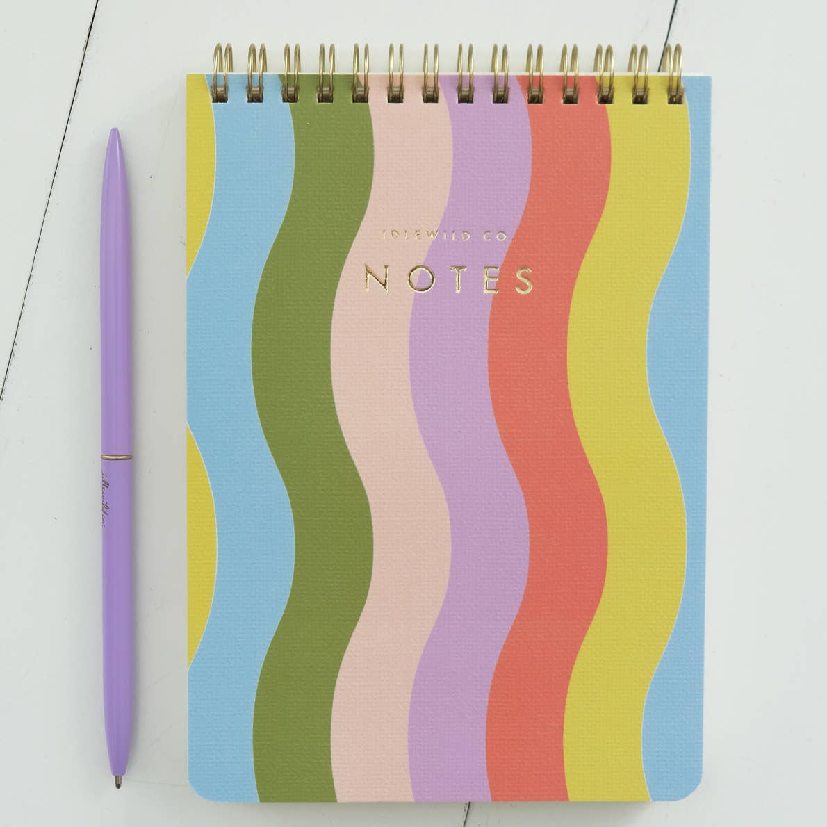 Notepad with blue, olive, pink, lilac, red, yellow and light blue vertical wavy lines with coil binding at top. 