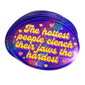 Decorative sticker with purple holographic background  and yellow text says, "The hottest people clench their jaws the hardest". 