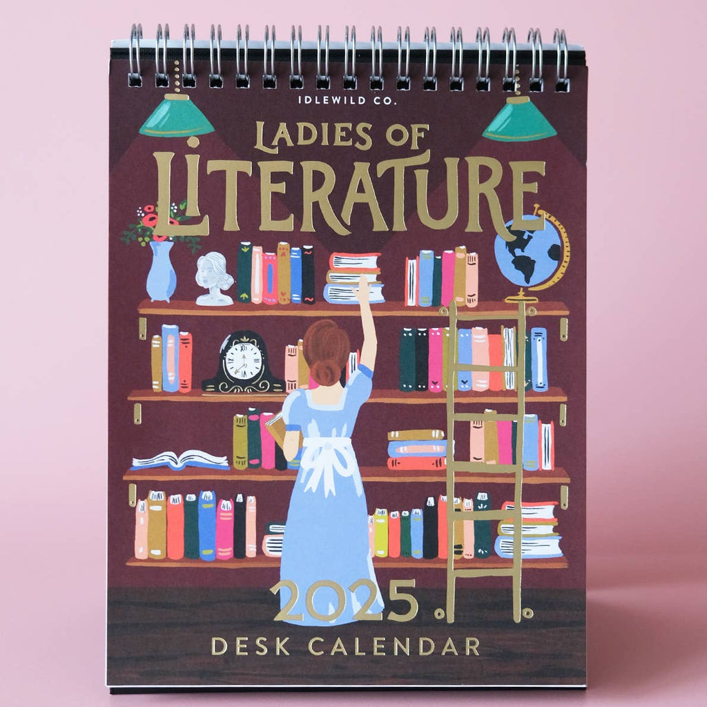 Calendar with burgundy background and image of bookshelves of books with woman stacking books, gold foil text says, "ladies of Literature, 2025 desk calendar". 